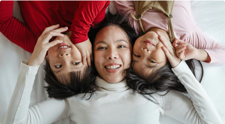 Mother and three children lying on the floor together, smiling and looking up at the camera.