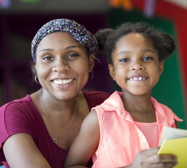 mother and daughter look up from reading a book together to face the camera