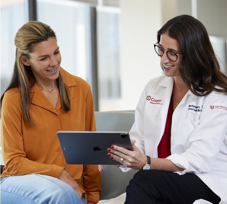 Female patient and female doctor sit side by side a doctor holds iPad an explains something to patient.