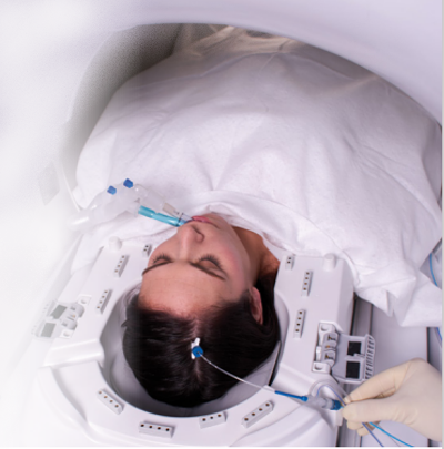 photograph shows a laser catheter positioned at the top right side of a woman's skull while she lies in an MRI machine