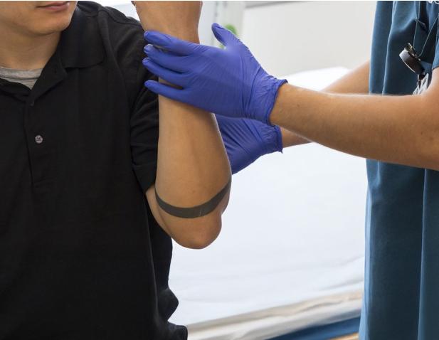 Healthcare provider wearing gloves positions a patient’s arm for an electromyography or nerve conduction study in a clinical setting.