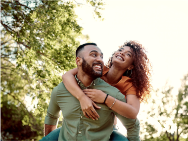 Smiling couple outdoors under a tree on a sunny day.