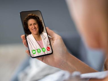 Close-up of a person holding a smartphone showing a video call with a doctor in a white coat.