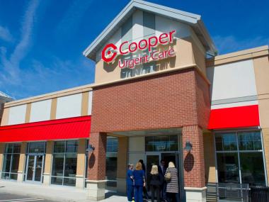 Exterior of Cooper Urgent Care building with red awnings and the Cooper logo above the entrance, on a sunny day.