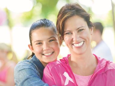 daughter hugs mother who is wearing a pink jacket with a white ribbon