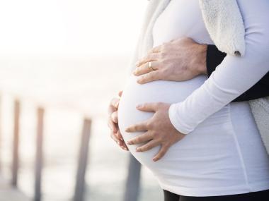woman holds her pregnant belly with her partner's hands also holding