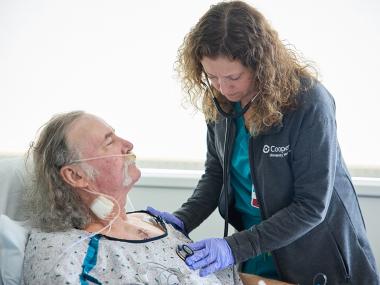 patient in hospital bed looks at with nurse associate with stethoscope
