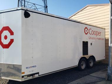 photo of large white trailer with Cooper University Health Care logo on it side