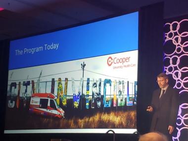 man stands on stage next to large presentation screen