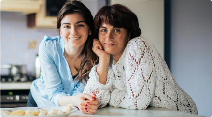 Mother and daughter smiling at the kitchen counter in a warm home setting.