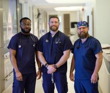 Three male nurses in navy scrubs stand in hospital hallway at Cooper Camden