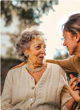 Older woman smiling and talking with a caregiver or family member outdoors.